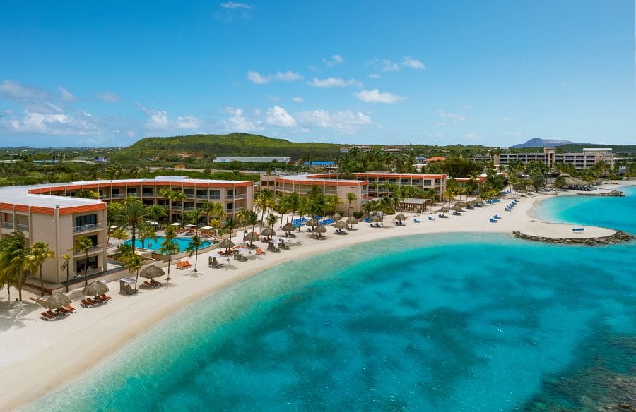 A stretch of beach, with resort buildings at Sunscape Curaçao Resort, Spa & Casino flanking the beach, at one of the best Curacao resorts with kids.