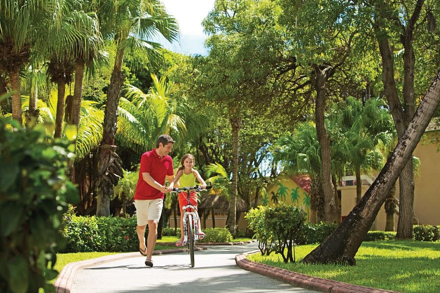 A dad helps his young daughter bike along a path at Sunscape Curaçao Resort, Spa & Casino.