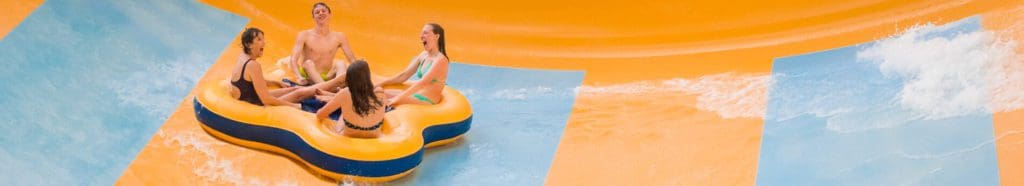 Four teens enjoy a waterslide together on a large orange tube at Water Country USA, one of the best water parks near Washington DC for families.