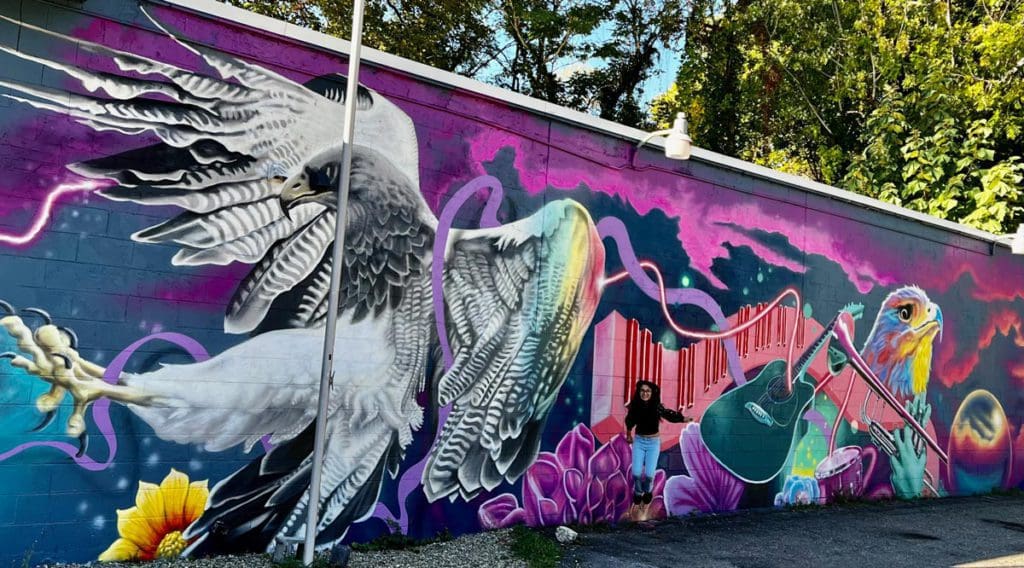 A young girl jumps in front of a vibrant graffiti mural in the Art District, a must stop on any Asheville family vacation itinerary.