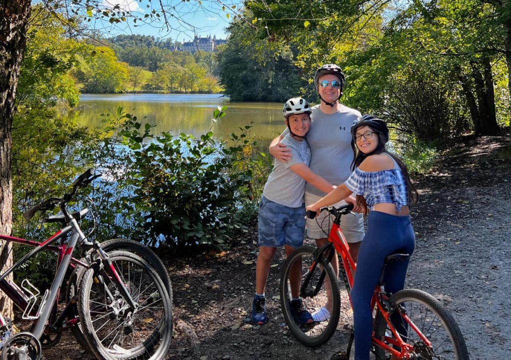 A dad and his two kids stand together with rented bikes nearby, as they explore the lush grounds of the Biltmore Estate.