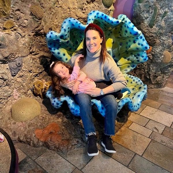 A mom and her young daughter sit together inside a giant clam chair.