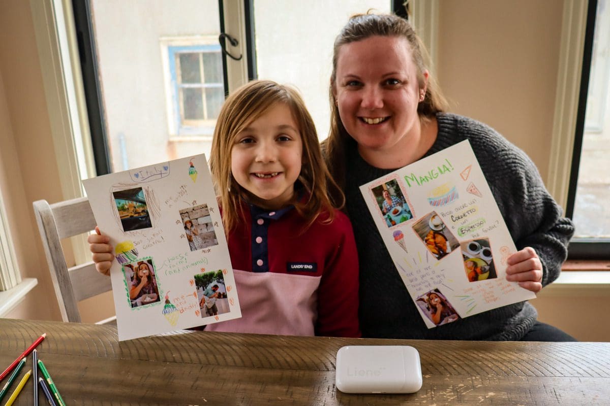 A mom and her young daughter proudly display the travel diary pages they created using the Liene Pearl Portable Photo Printer.