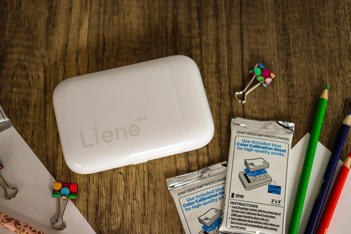 A product shot of a Liene Pearl Portable Photo Printer from overhead, near several scrapbooking supplies, including colored pencils.