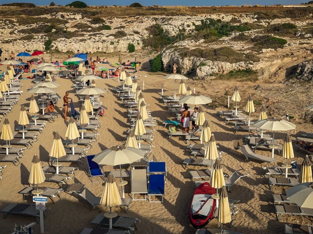An aerial view of a lido in Puglia, filled with open white umbrellas on the beach.