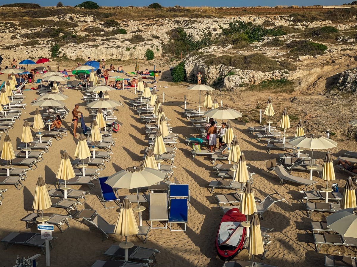 An aerial view of a lido in Puglia, filled with open white umbrellas on the beach, knowing what to do is one of the essential tips for visiting Puglia with kids.