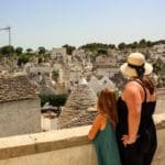 A mom and her young daughter stand together overlooking a scenic view of the traditional trulli of Alberobello.