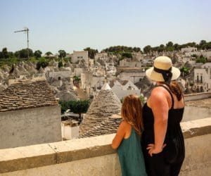 A mom and her young daughter stand together overlooking a scenic view of the traditional trulli of Alberobello.
