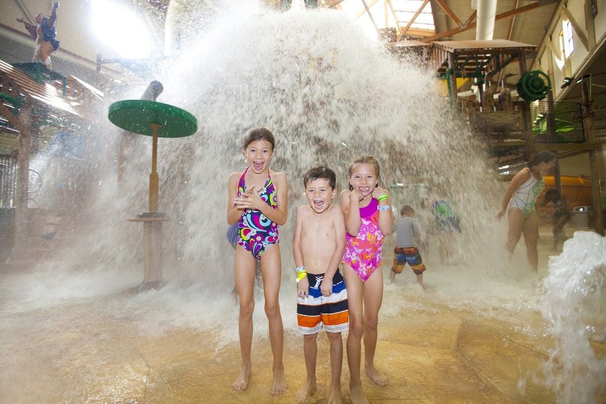 Three kids stand together under a large spray of water at Great Wolf Lodge Grapevine.