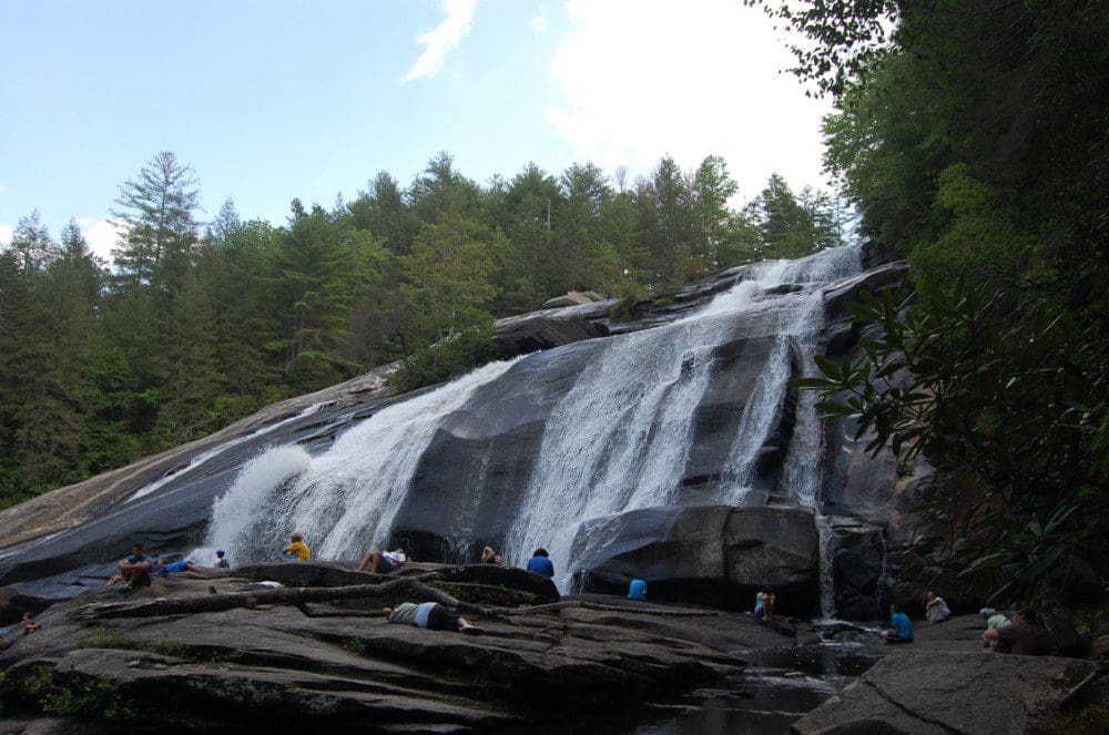 A view of the waterfall at DuPont State Forest, with people exploring the base.