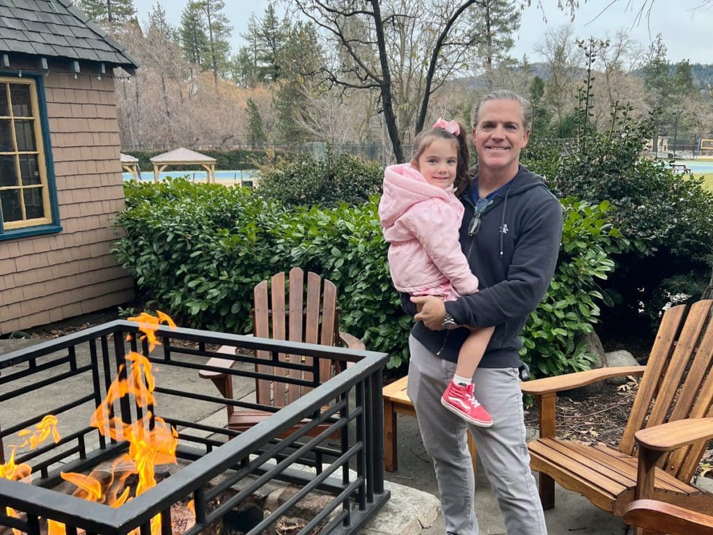 A dad and his young daughter pose together near a fire pit at UCLA Lake Arrowhead Lodge.
