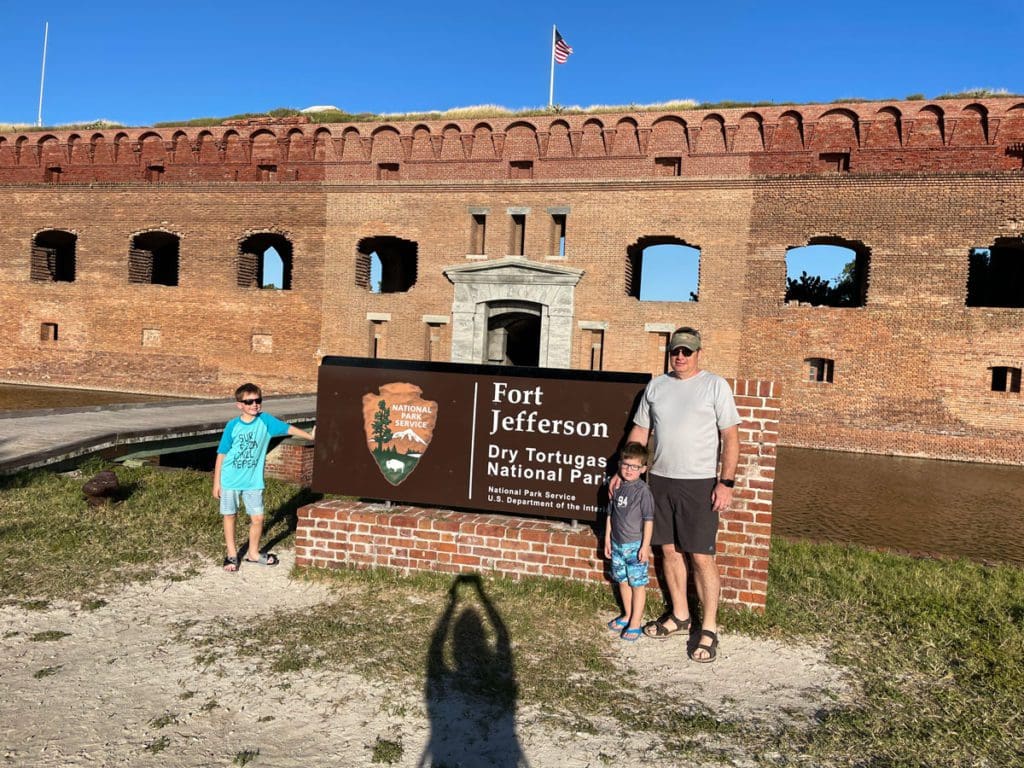 A dad and his two young boys stand near the entrance sign to Dry Tortugas National Park.