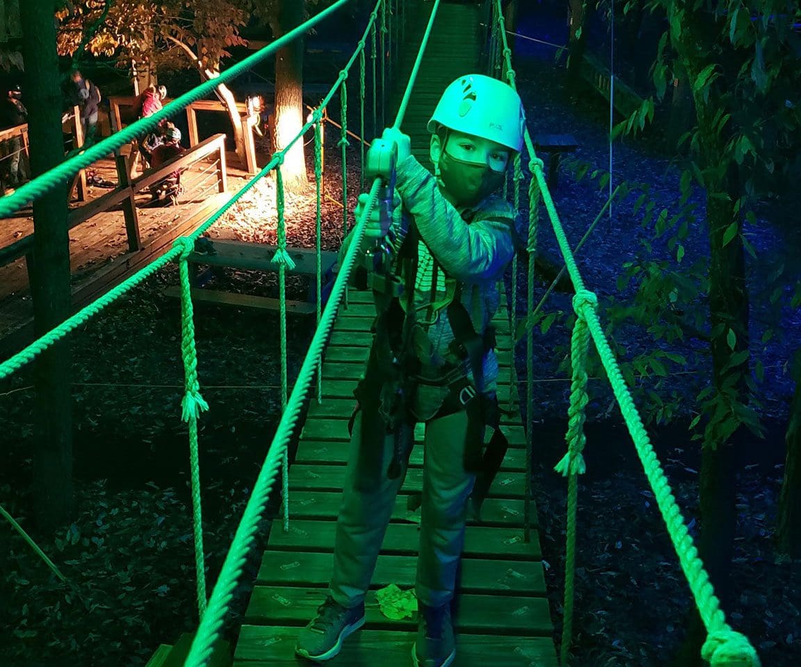 A young boys makes his way along a night zipline path in Asheville.
