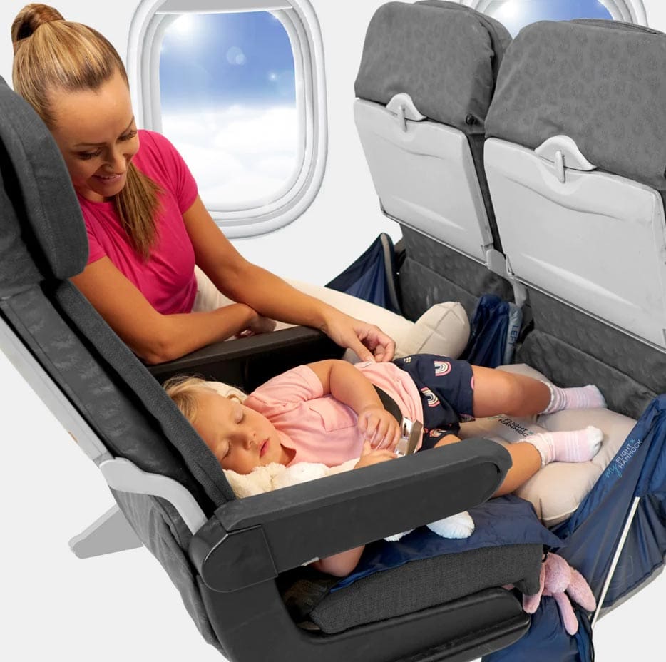 A mom looks on as her young daughter sleeps on a plane using the My Flight Hammock.