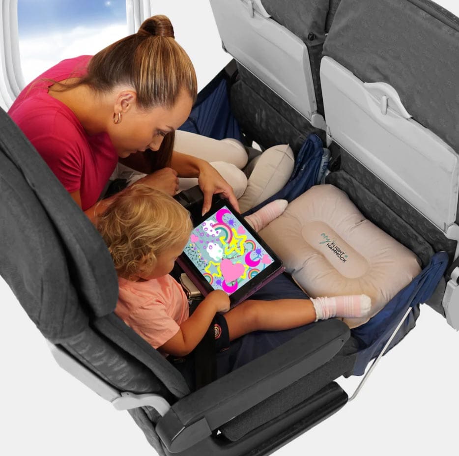 A mom and her young daughter use the My Flight Hammock from Fly Legs Up Hammock on a plane, one of the best products for sleeping on long international flights with kids.