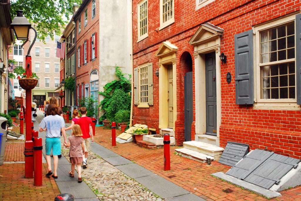 A family of three walks down a historic street in Philadelphia together, one of the best Labor Day Weekend getaways near DC for families.
