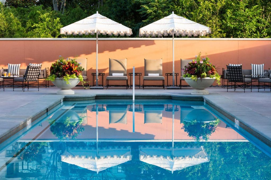 Lovely chairs and umbrellas flank the outdoor pool at Rosewood Mansion on Turtle Creek, one of the best hotels in Dallas for families.