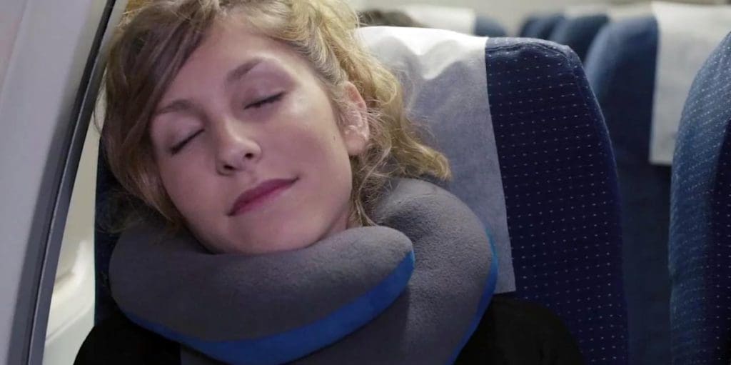 A sleeping woman uses the BCOZZY Chin Supporting Travel Pillow on a flight, this is one of the best products for sleeping on long international flights with kids.