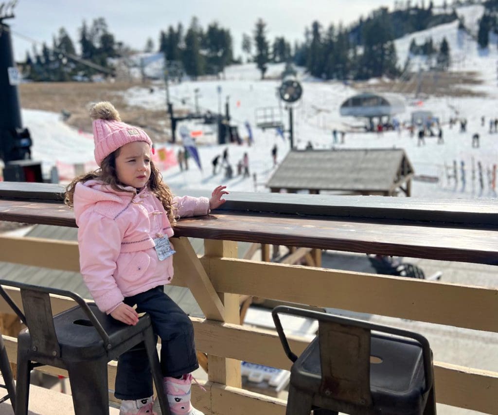 A young girl sits on an outdoor patio overlooking a California ski area.