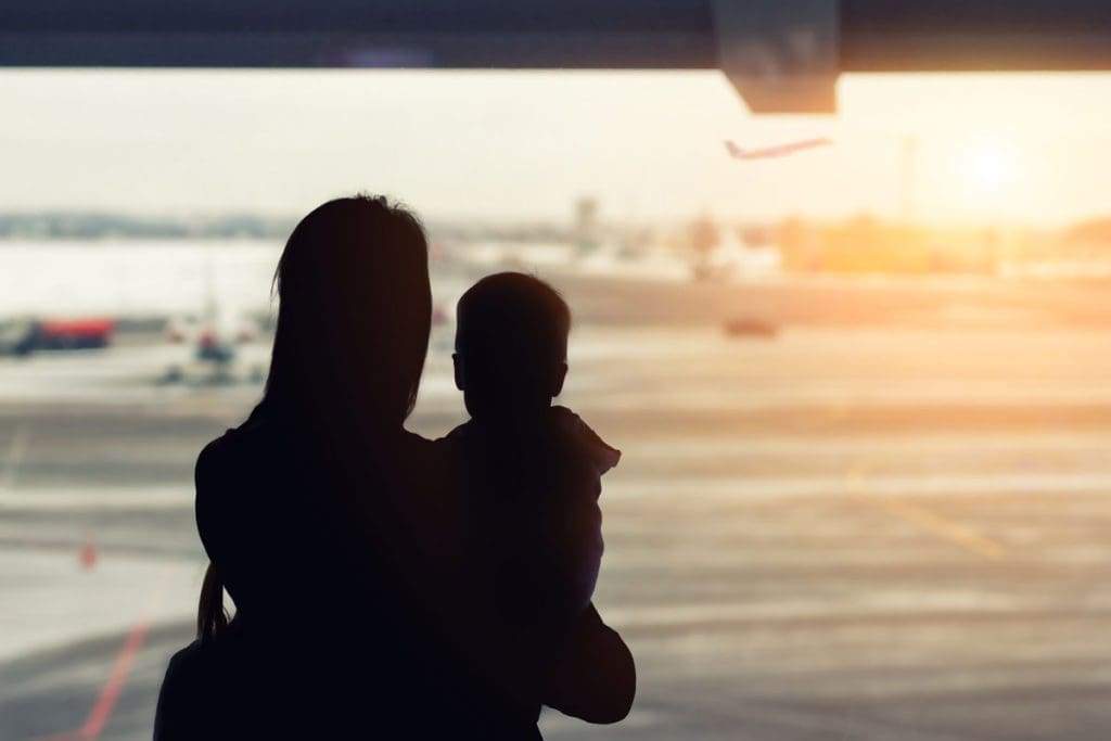 The silhouette of a woman holding her baby watching planes take off at an airport.