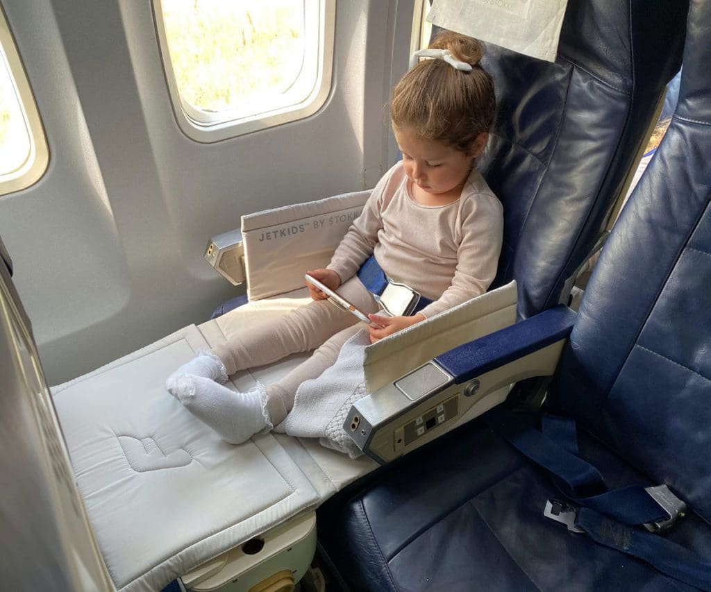 A young girl sits on a plan in her JetKids by Stokke, allowed by JetBlue Airlines' policies for kids.