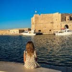 A young girl sits on a bench in the old sea port of Monopoli looking out onto the old city walls.