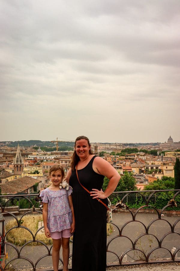 A mom and her daughter stand together with an expansive view of Rome behind them.