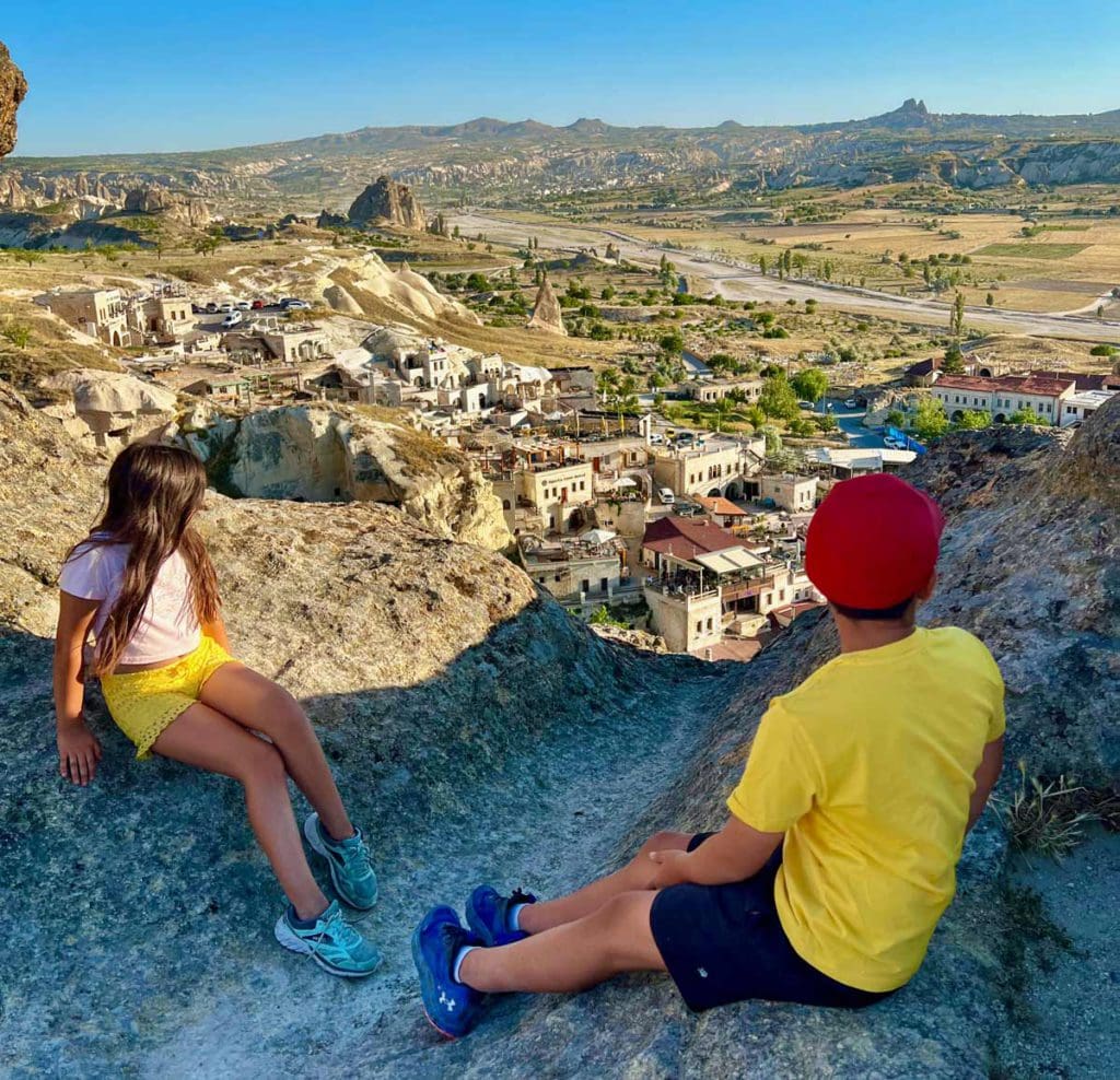 Two kids sit on a rock formation, overlooking an ancient city in Cappadocia.
