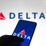 A hand navigates the Delta app with the Delta logo in the background.
