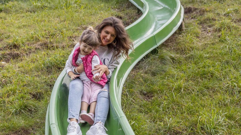 A mom and her young daughter slide down an outdoor slide at Family Hotel Adriana.