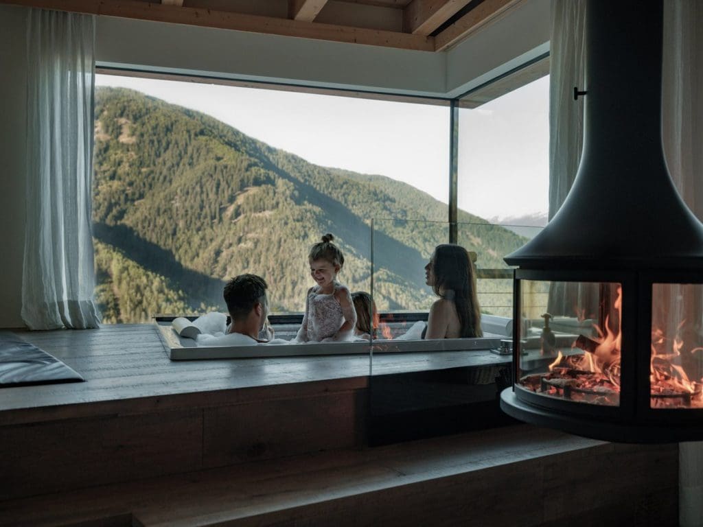 A family of four enjoys an afternoon in a hot tub with a view of the mountains, while staying at Familyhotel Sonnwies Dolomites, one of the best all-inclusive resorts In Italy for families.