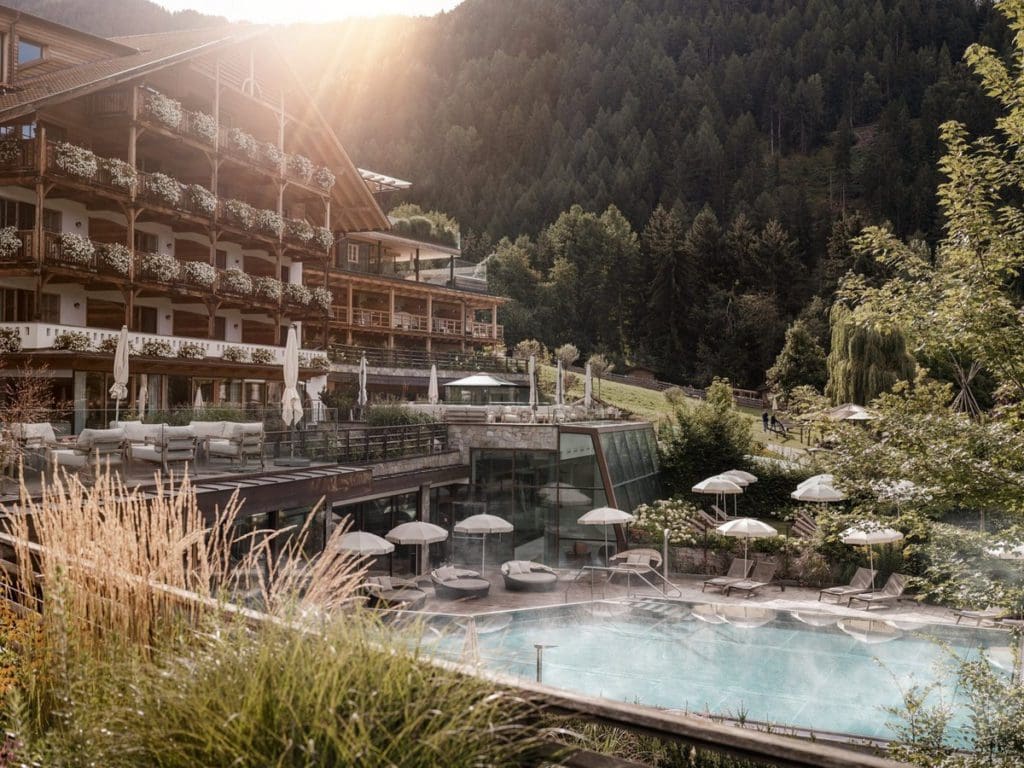 The rear exterior of Familyhotel Sonnwies Dolomites with an outdoor pool and woodsy grounds at one of the best all-inclusive resorts In Italy for families.