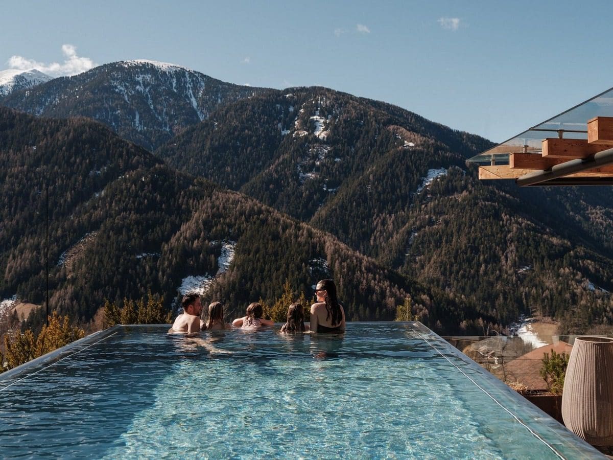 A family enjoys an outdoor pool on a sunny day at Familyhotel Sonnwies Dolomites.