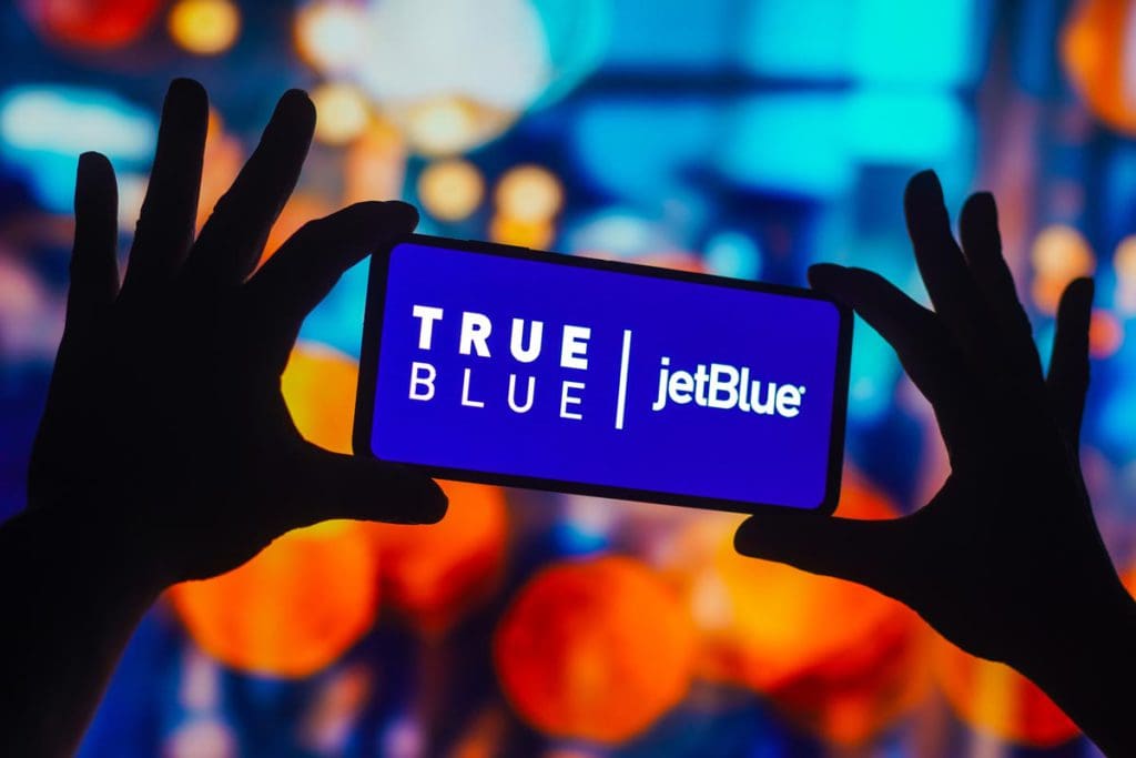 Two hands hold up a phone reading the JetBlue Airlines app, helpful when flying with kids.