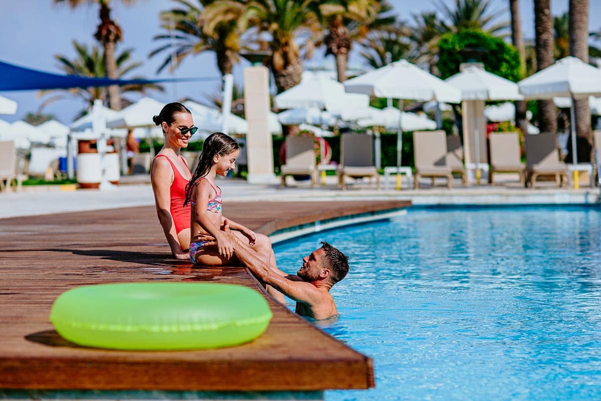 A family of three sits poolside, while enjoying a beautiful day in Cyprus.