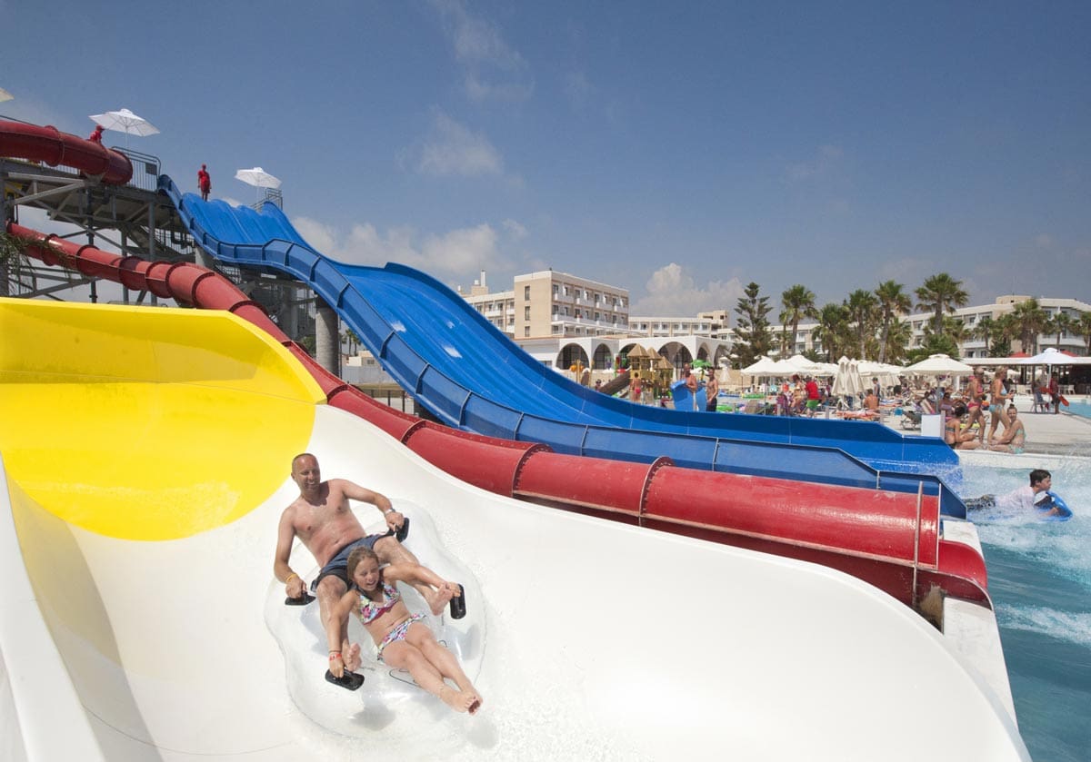 A father and daughter ride down a water slide on a tube at Louis Phaethon Beach Resort, one of the best all-inclusive resorts in Cyprus for families.