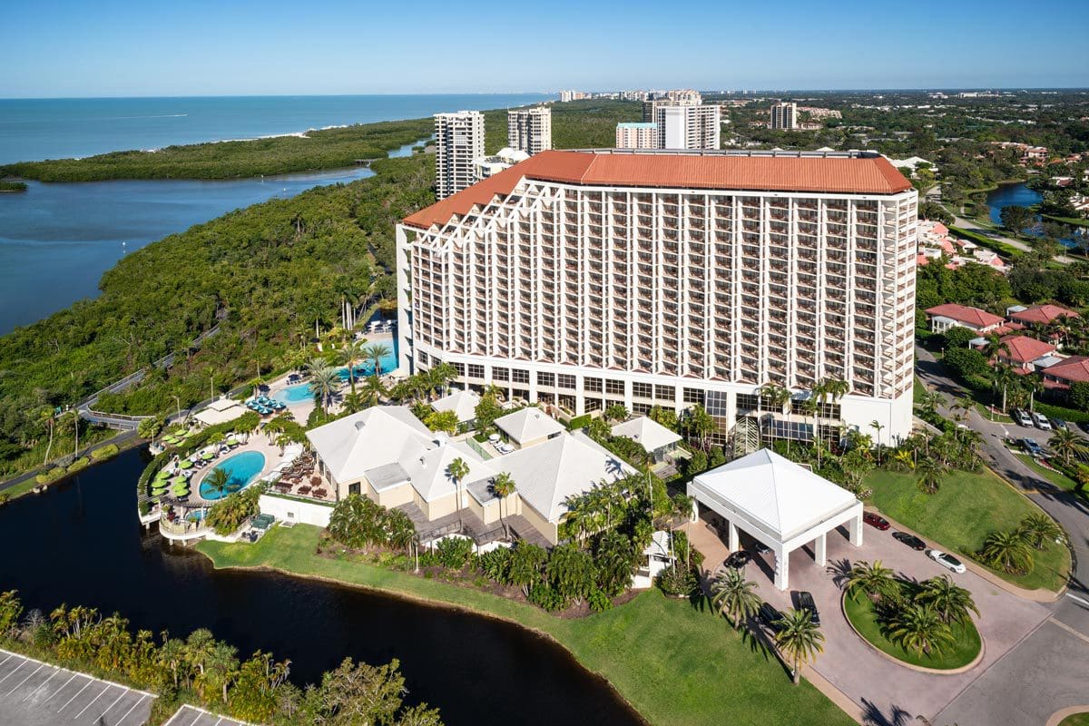 An aerial view of Naples Grande Beach Resort near the beach on a sunny day.