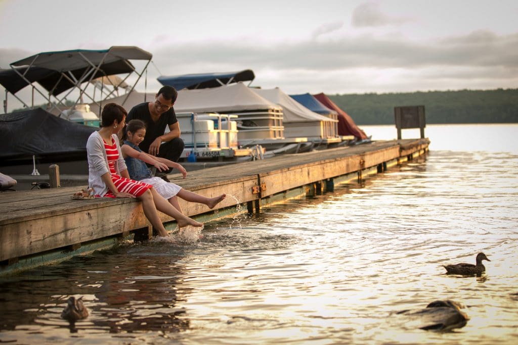 A family enjoys feeding the ducks from a dock at sunset on Lake Wallenpaupack, one of the best lakes for a family vacation within 4 hours of NYC.