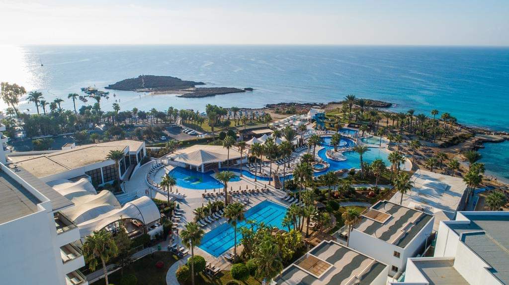 An aerial view of the pool and surrounding resort grounds, with the ocean in the distance, at Adams Beach Hotel, one of the best all-inclusive resorts in Cyprus for families.