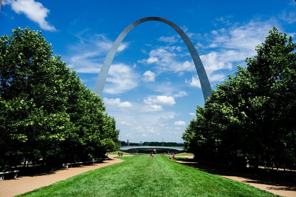 The St. Louis Arch beyond fully leafed summer trees in St. Louis, Missouri, one of the best affordable summer vacations in the United States with kids.