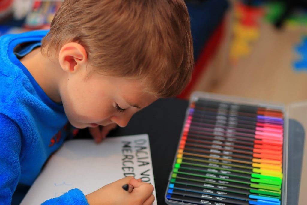 A young boy writes on a piece of paper with markers.