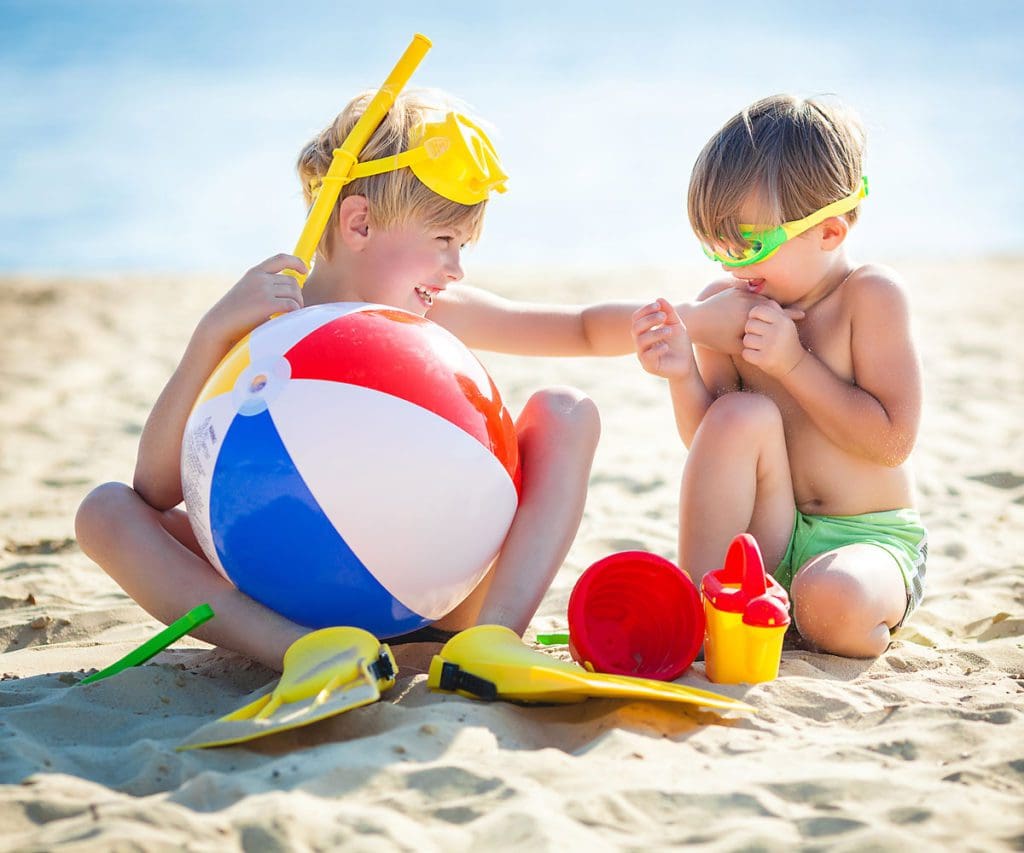 Two kids playing on the beach together with beach toys, which are a must on a beach packing list for families.