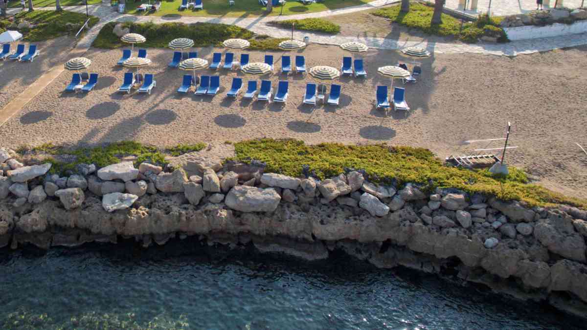 An aerial view of the beach, with beach loungers and umbrellas, at Leonardo Cypria Bay Hotel.