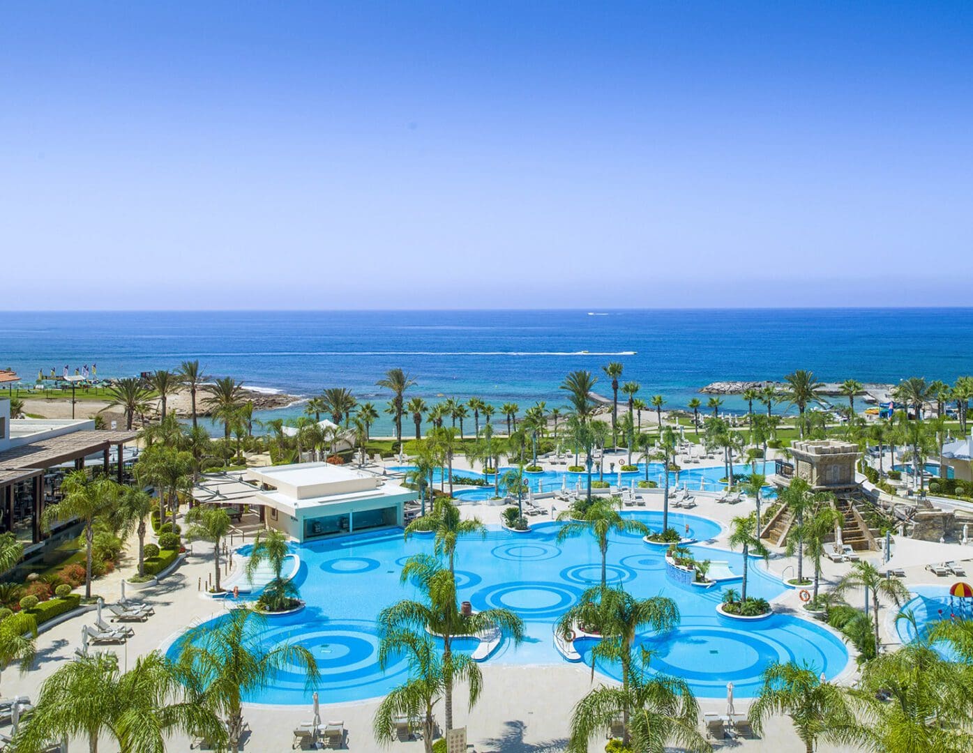 The pristine pool, surrounded by palm trees, with the beach in the distance at Olympic Lagoon Resorts, Paphos.