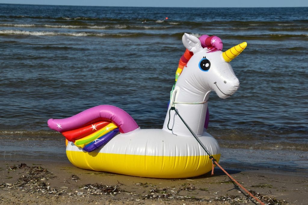 A unicorn floatie rests on the sand near the water.