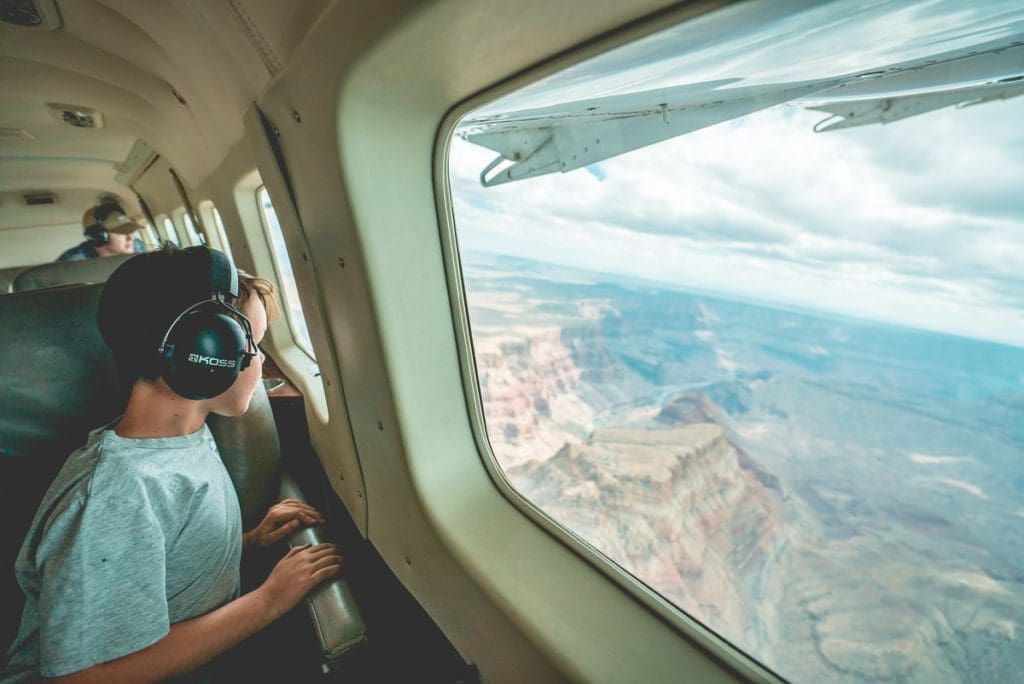 A young boy wearing headphones looks out a plane window onto a desert scene.