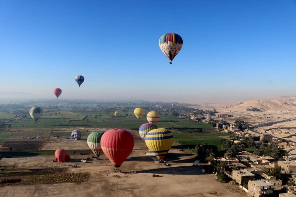 Several hot air balloons move over the landscape below near Luxor, a must-do activity on this 2-Week Egypt Itinerary for Families.
