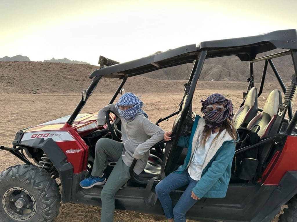 Two kids, wearing scarves, sit in a vehicle while on a desert tour in Egypt.