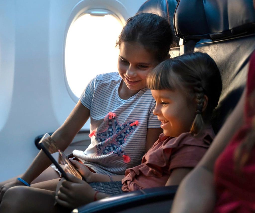 Two kids play a game on an iPad together on an airplane.