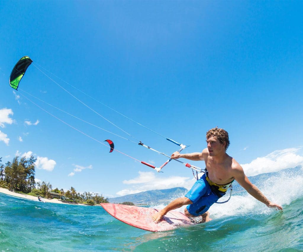 A teen boy kite-surfs in blue ocean waves.